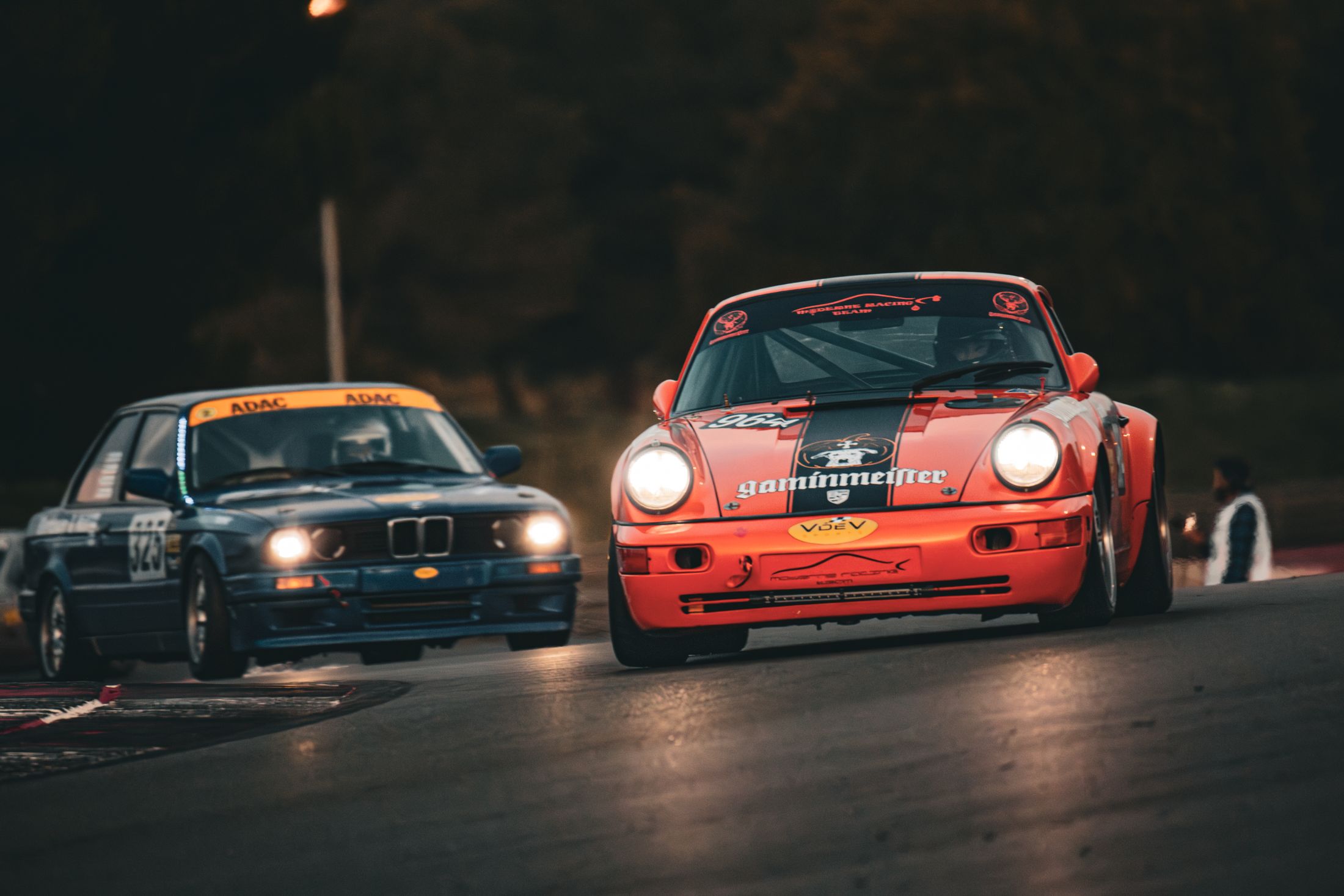 BMW noire et Porsche orange côte à côte, course de nuit