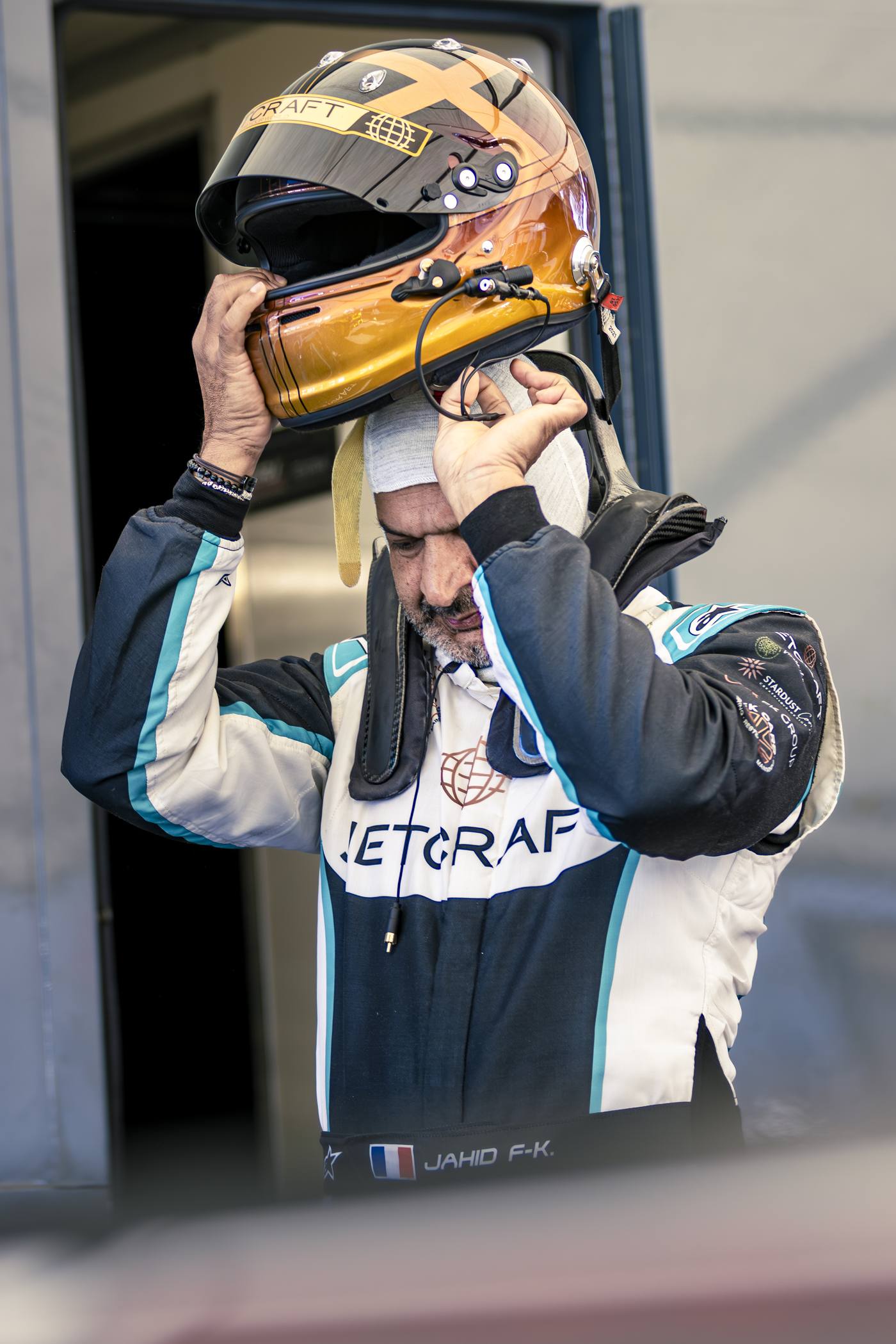 Pilote JetCraft Jahid F-K enfilant casque or devant le stand, combinaison bleue, Paul Ricard 2026