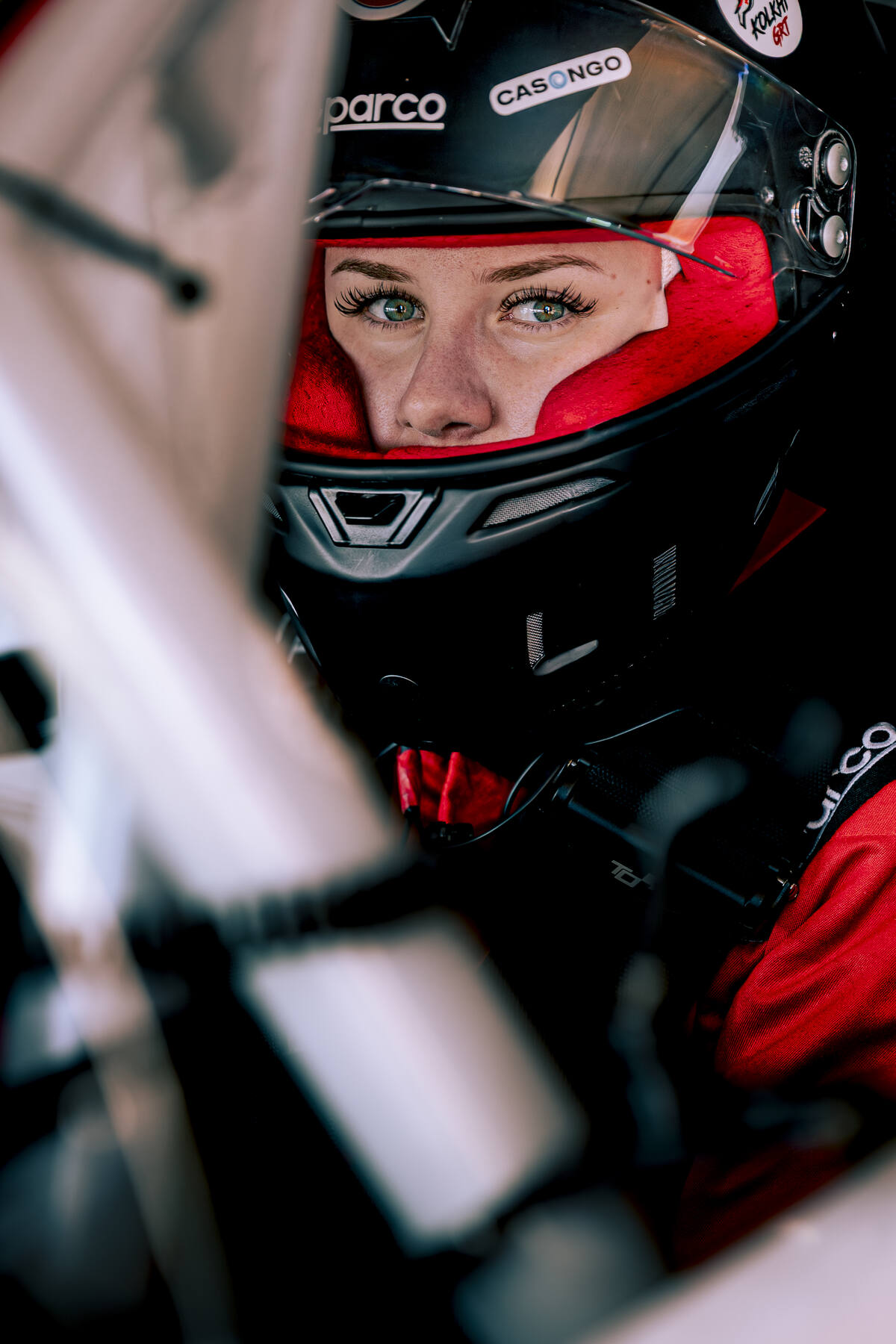 Portrait femme pilote NASCAR casque Sparco rouge et noir, regard intense à travers la visière, Paul Ricard 2026