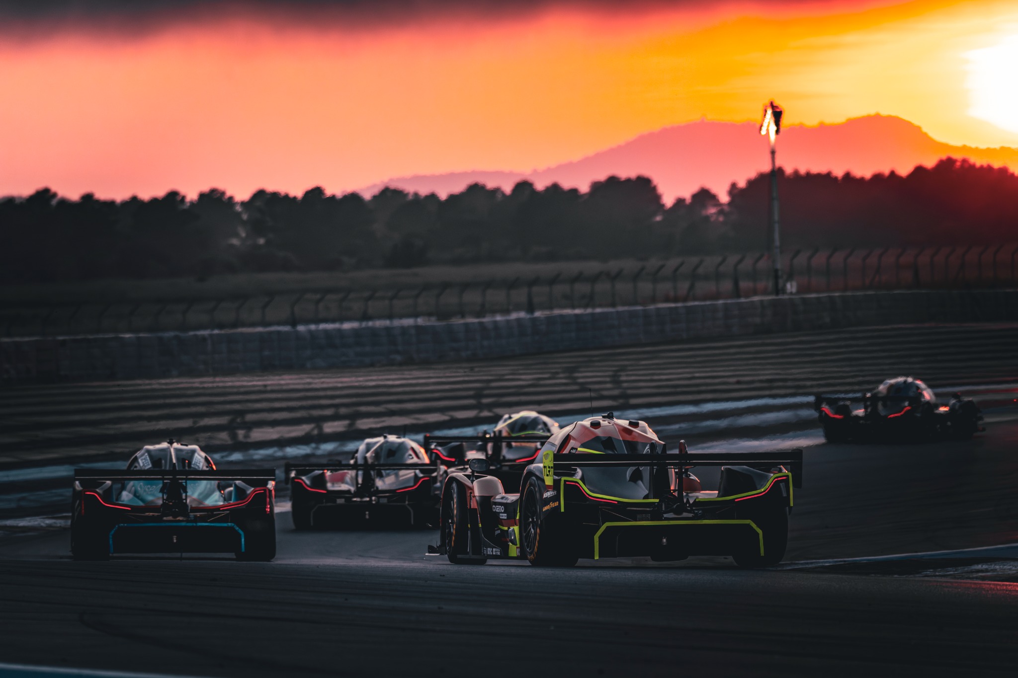 Peloton de prototypes d’endurance vu de dos sous un ciel rouge au coucher du soleil