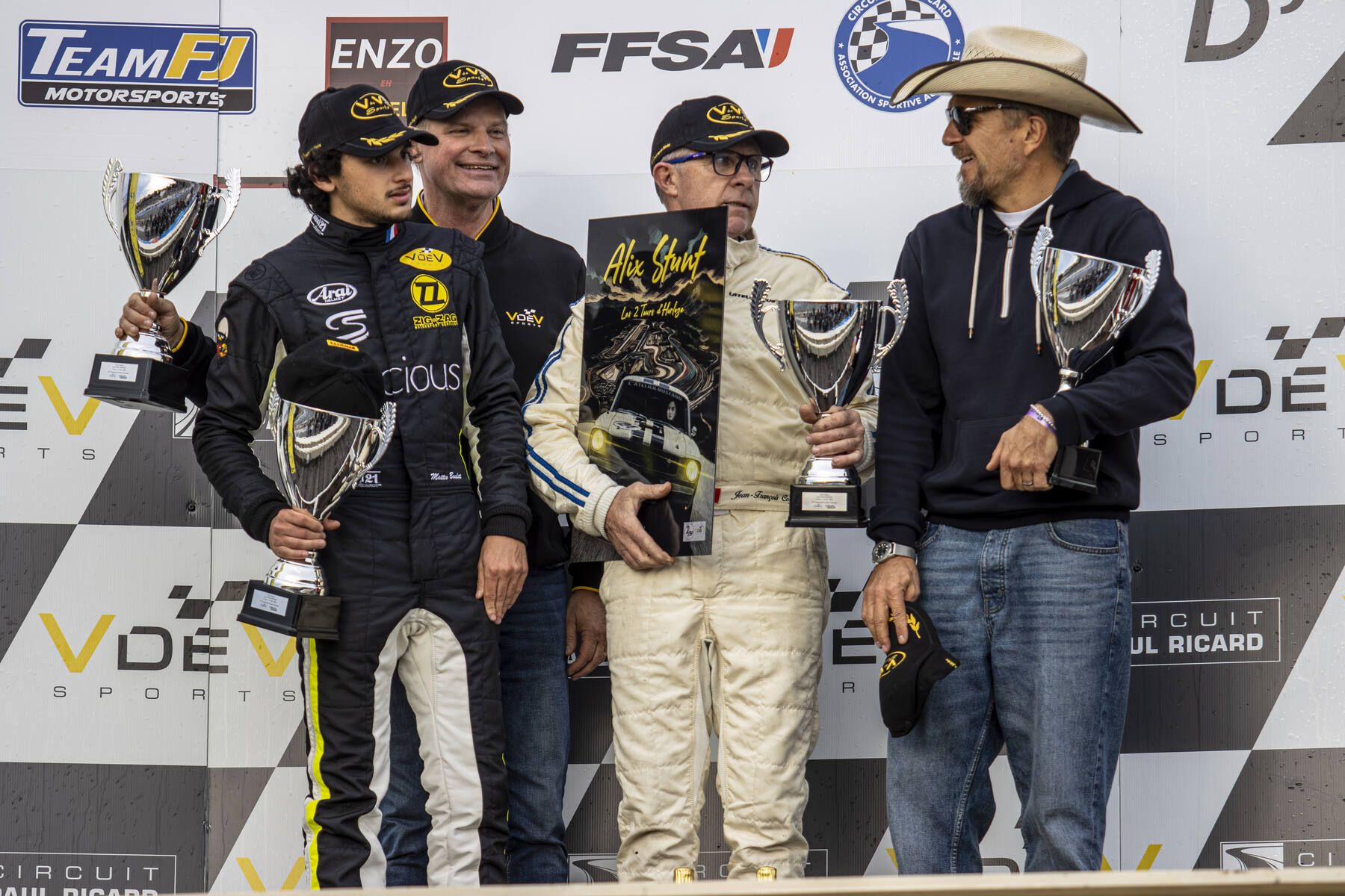 Podium des 2 Tours d'Horloge 2025 avec Jean-François Gagick en combinaison blanche tenant le livre Alix Stunt, accompagné de J.-P. Gagick au chapeau de cowboy et de Mattia Baldi