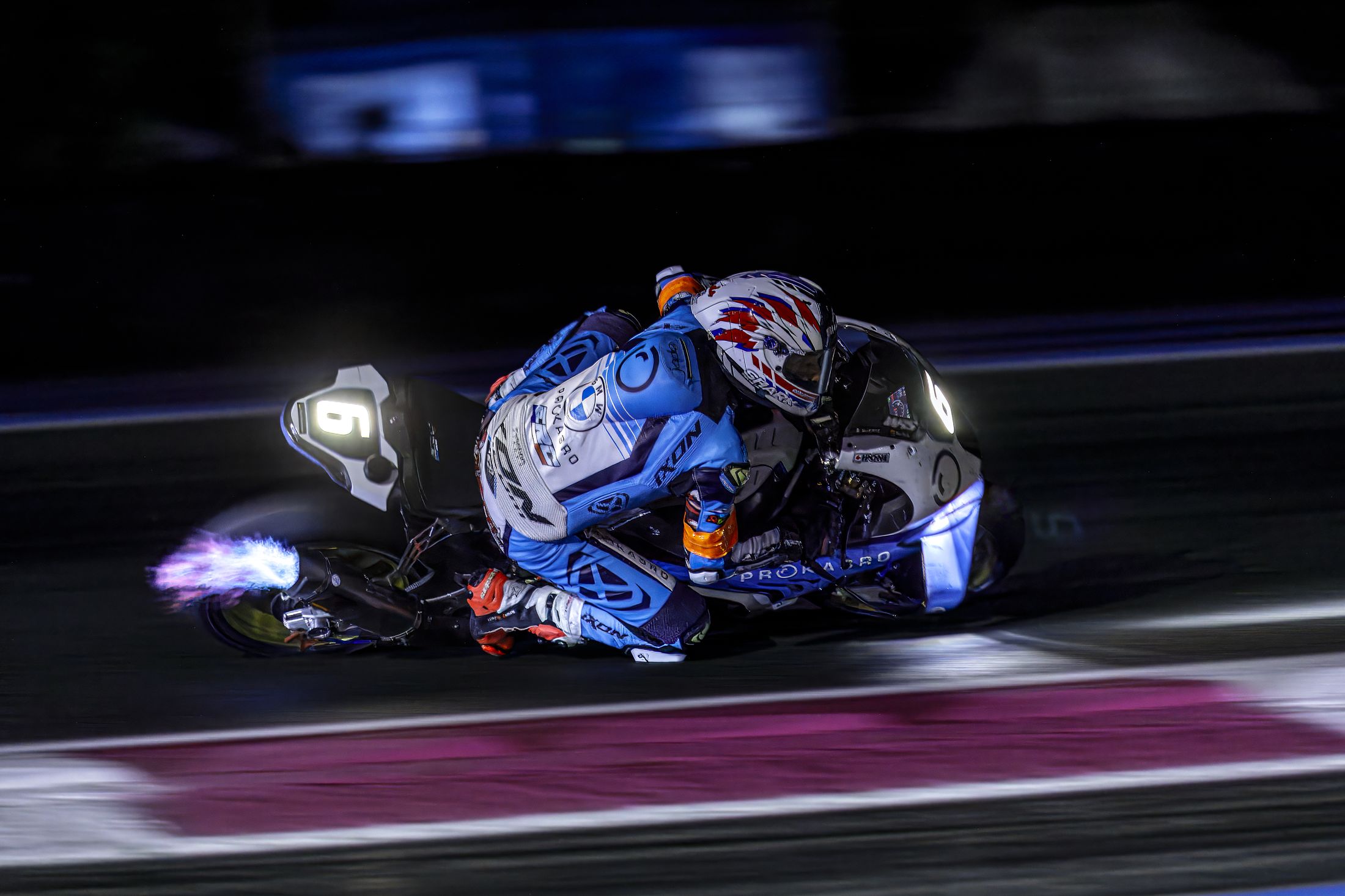 Pilote moto en pleine inclinaison de nuit, flamme à l'échappement