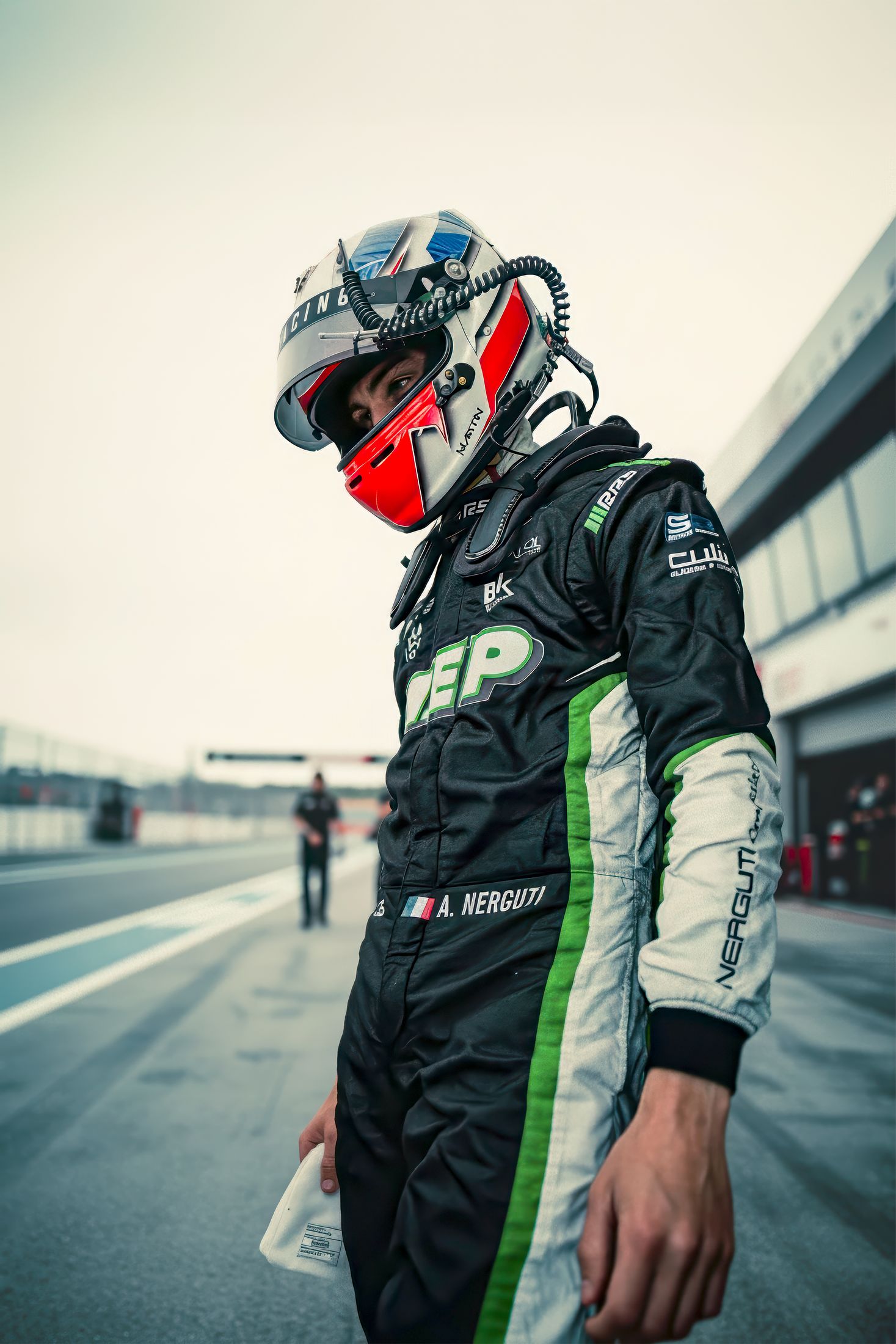 Pilote debout dans la voie des stands, casque à la main, lumière du soir