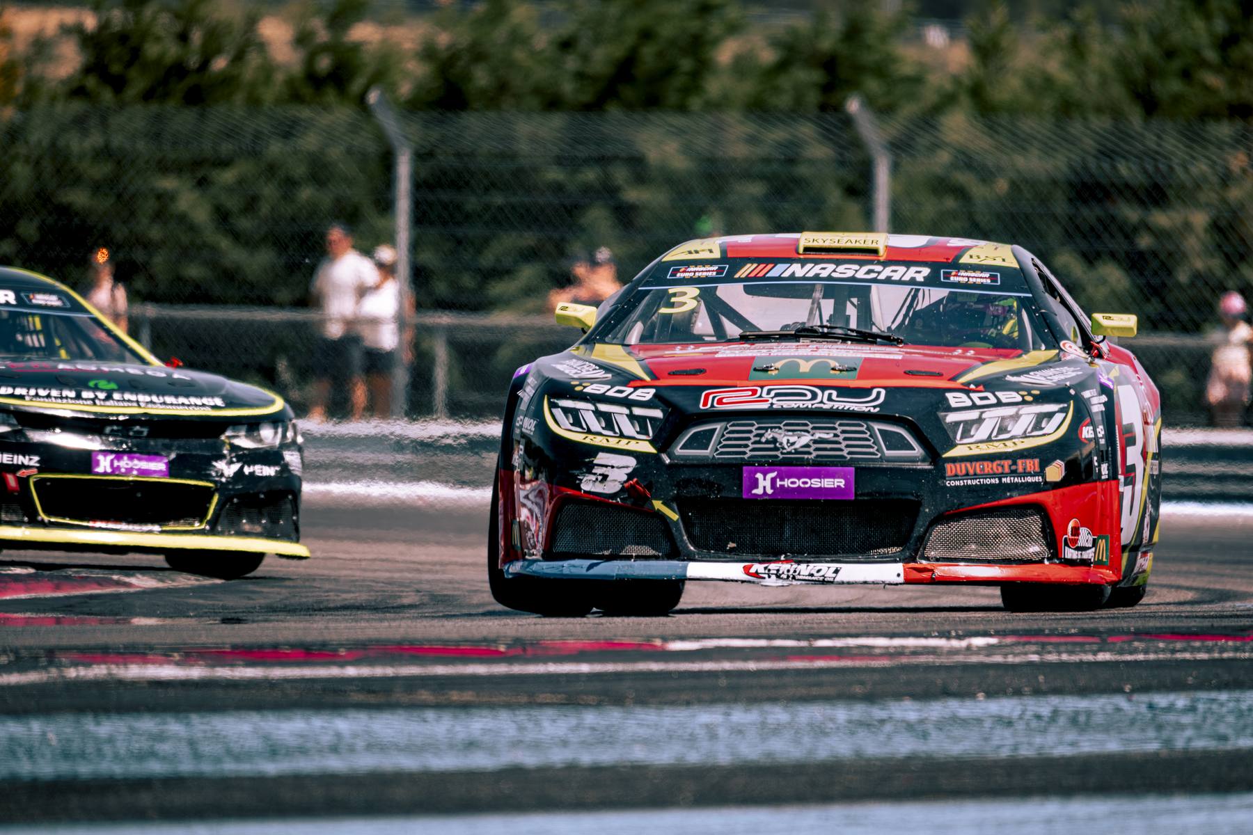 Stock-car noir et rouge, plan serré de face en virage