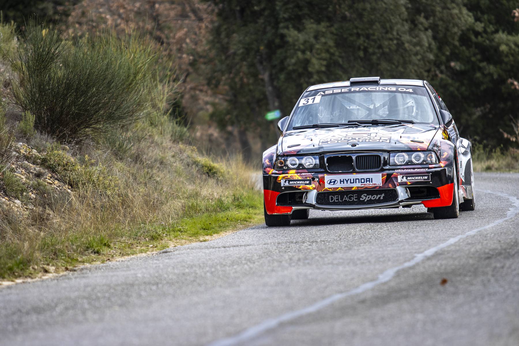 BMW noire et rouge en plein virage, route de montagne